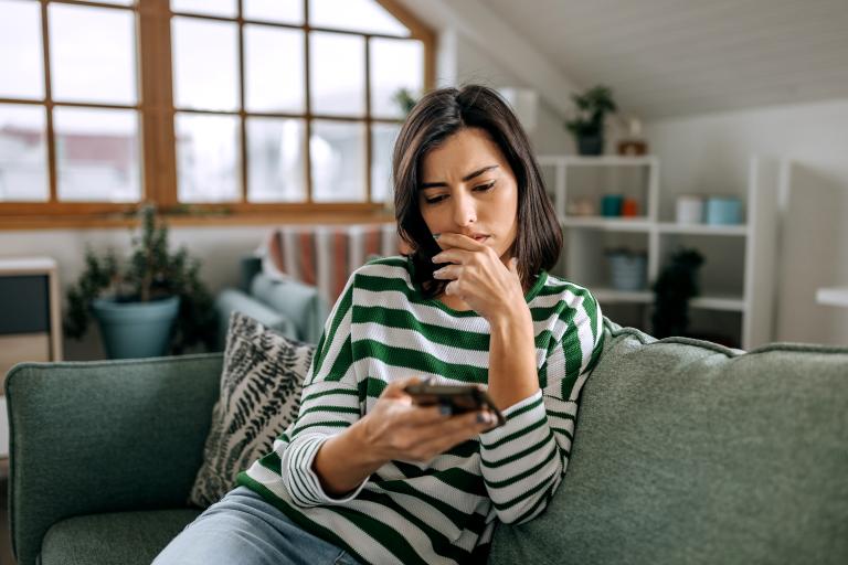 Vrouw zit met smartphone op de bank en kijkt verschrikt