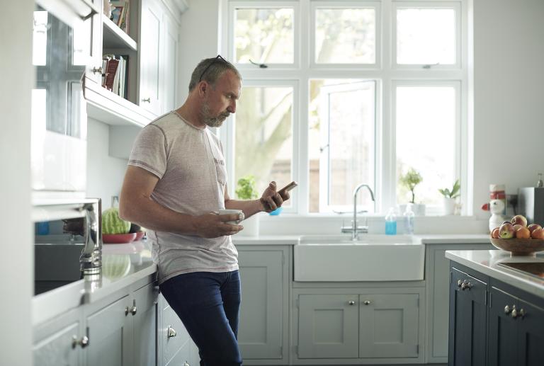 Man staat met telefoon in keuken