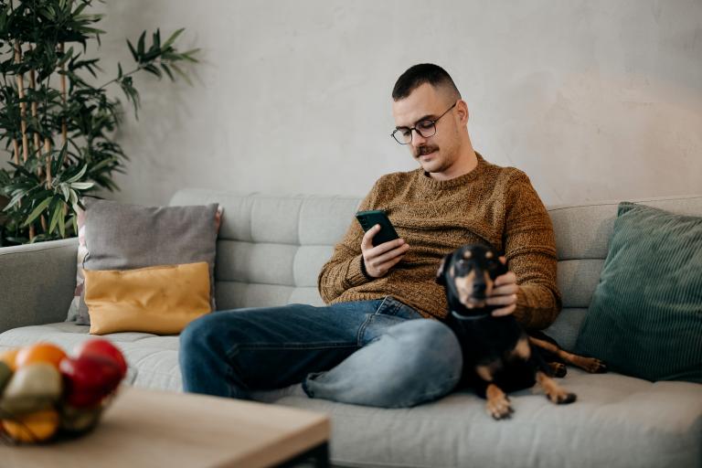 Man zit met smartphone en hond op de bank